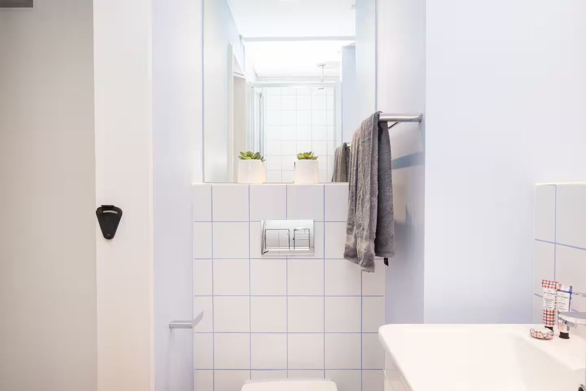 A clean and functional bathroom featuring a wall-mounted toilet with a concealed cistern, tiled splashback, vanity basin, and a large wall mirror.