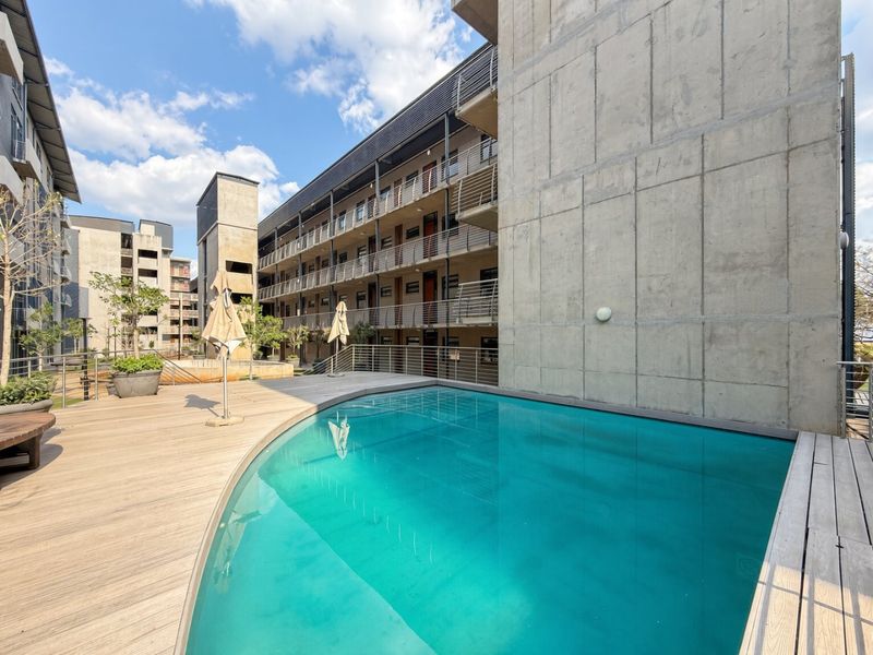 A modern apartment complex pool area featuring a swimming pool with timber decking and exposed concrete architectural elements.