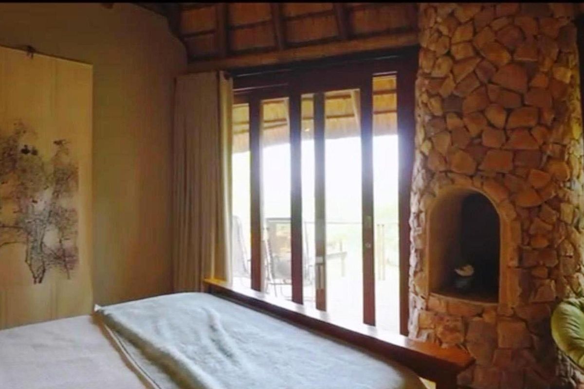A bedroom featuring a unique stone-clad fireplace, high thatched ceiling, and large sliding glass doors that open onto an outdoor patio area.