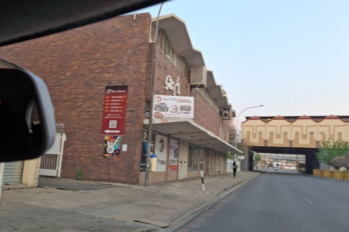 Street-level view of a commercial brick building featuring an awning and exterior air conditioning unit, situated along a public road.