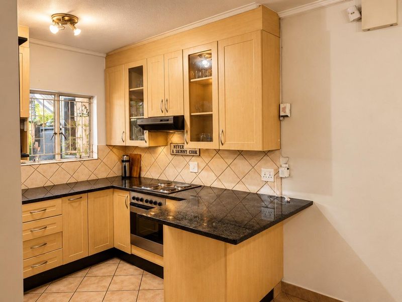 A functional kitchen featuring light-wood cabinetry, dark granite countertops, built-in oven, electric hob, and tiled finishes.