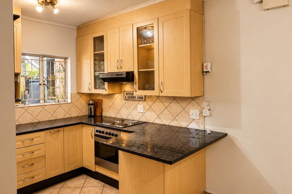 A functional kitchen featuring light-wood cabinetry, dark granite countertops, built-in oven, electric hob, and tiled finishes.