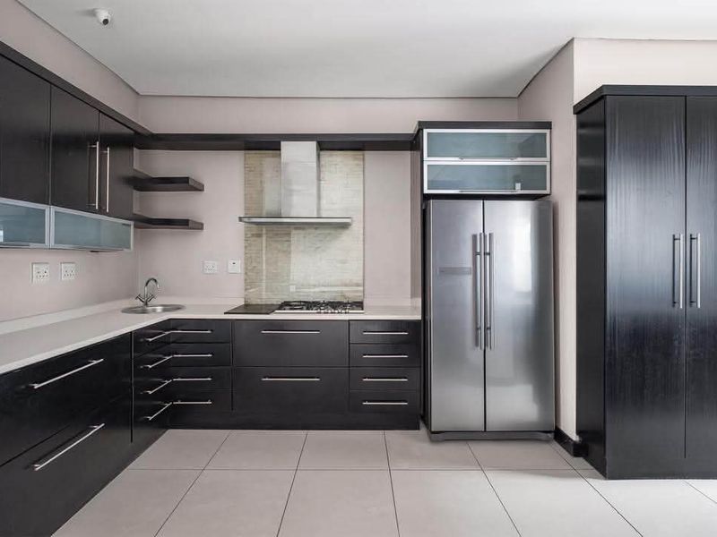 Modern kitchen featuring dark wood cabinetry, stone countertops, stainless steel appliances, and tiled flooring in a clean, contemporary layout.