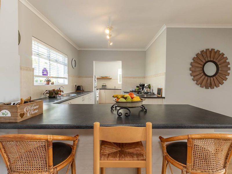 A functional kitchen featuring a central island with a dark countertop, ample cabinetry, and a tiled backsplash, opening into a secondary prep area.