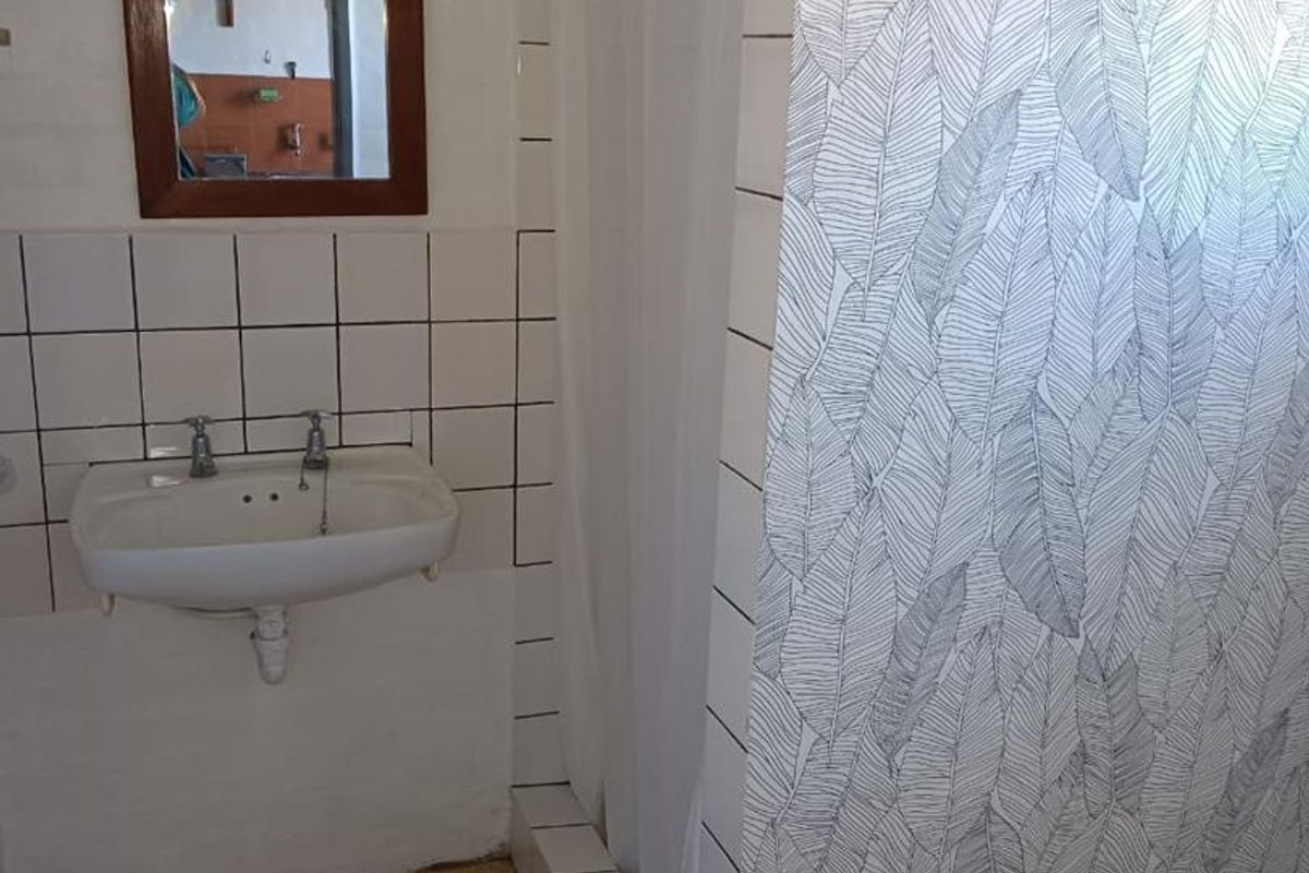 A functional bathroom featuring a wall-mounted basin, tiled splashback, and a shower enclosure with a curtain.