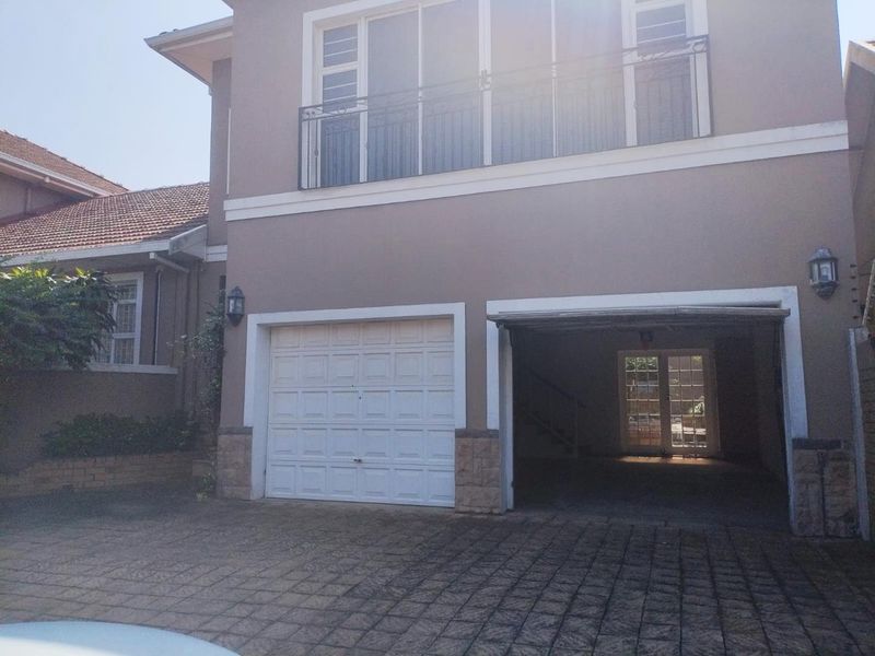Front elevation of a two-story house featuring a double garage, paved driveway, and an upper-level balcony with wrought iron railings.