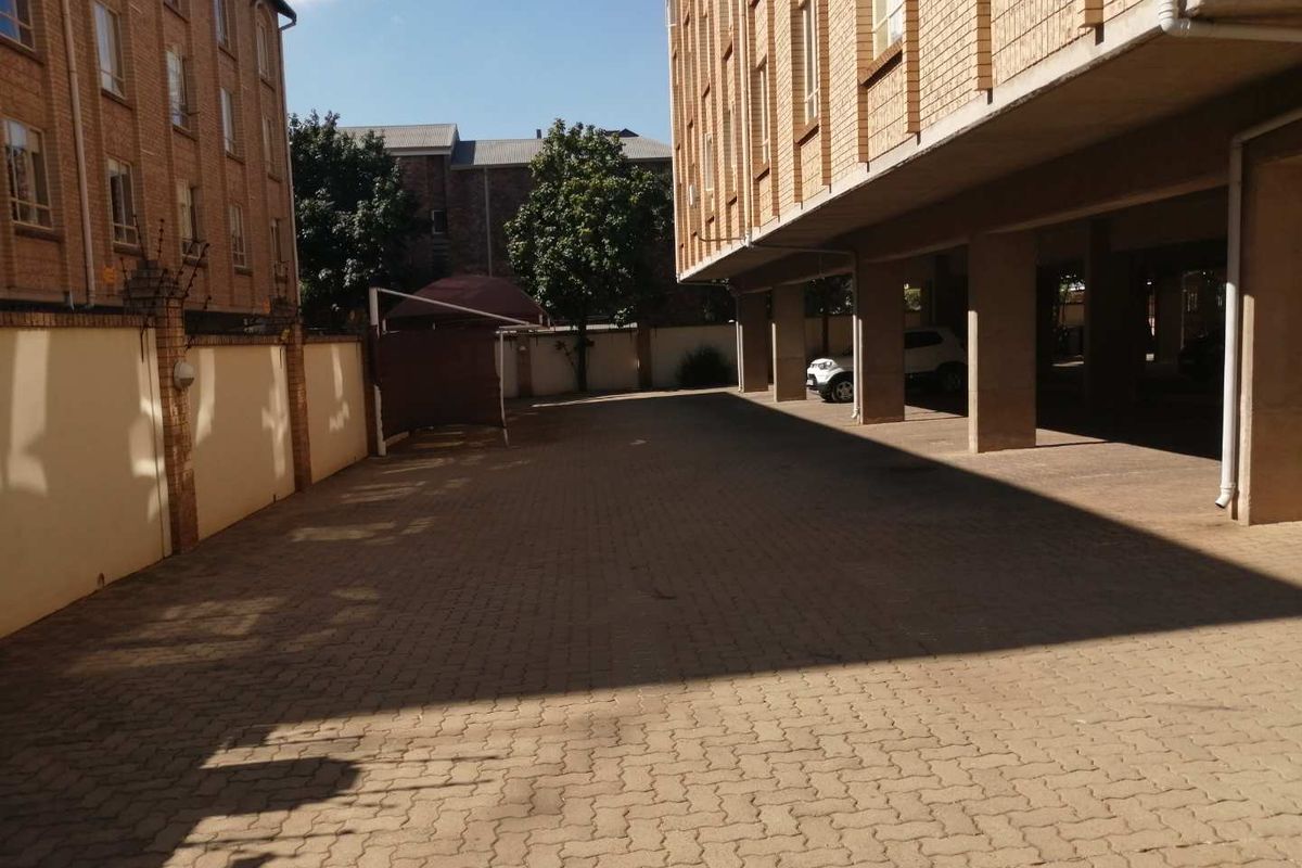 A paved exterior rear parking area featuring covered parking bays supported by concrete pillars and enclosed by a brick boundary wall.