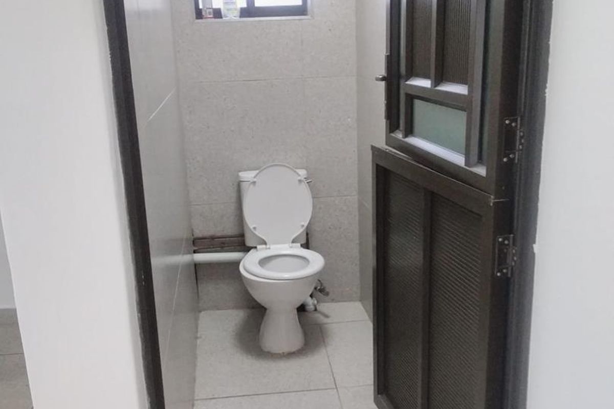 A compact, functional bathroom featuring tiled walls and flooring, a standard toilet, and an aluminium door.