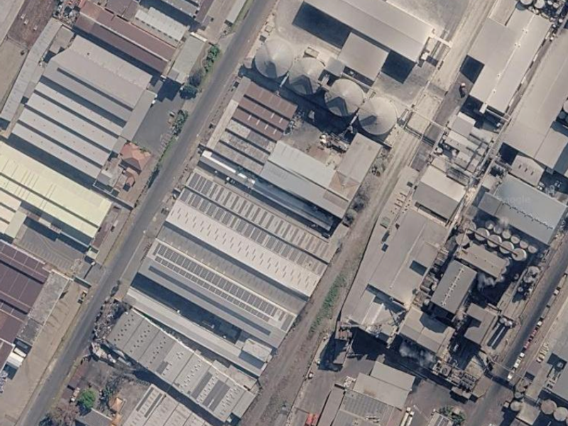 Aerial view of a large industrial facility featuring multiple warehouse structures, silo storage units, and extensive solar panel installations on the roof.