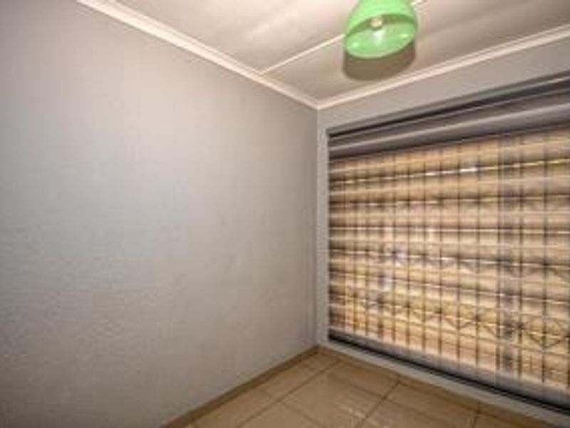 A clean, empty bedroom featuring neutral wall finishes, tiled flooring, and fitted roller blinds, providing a versatile space ready for personalization.