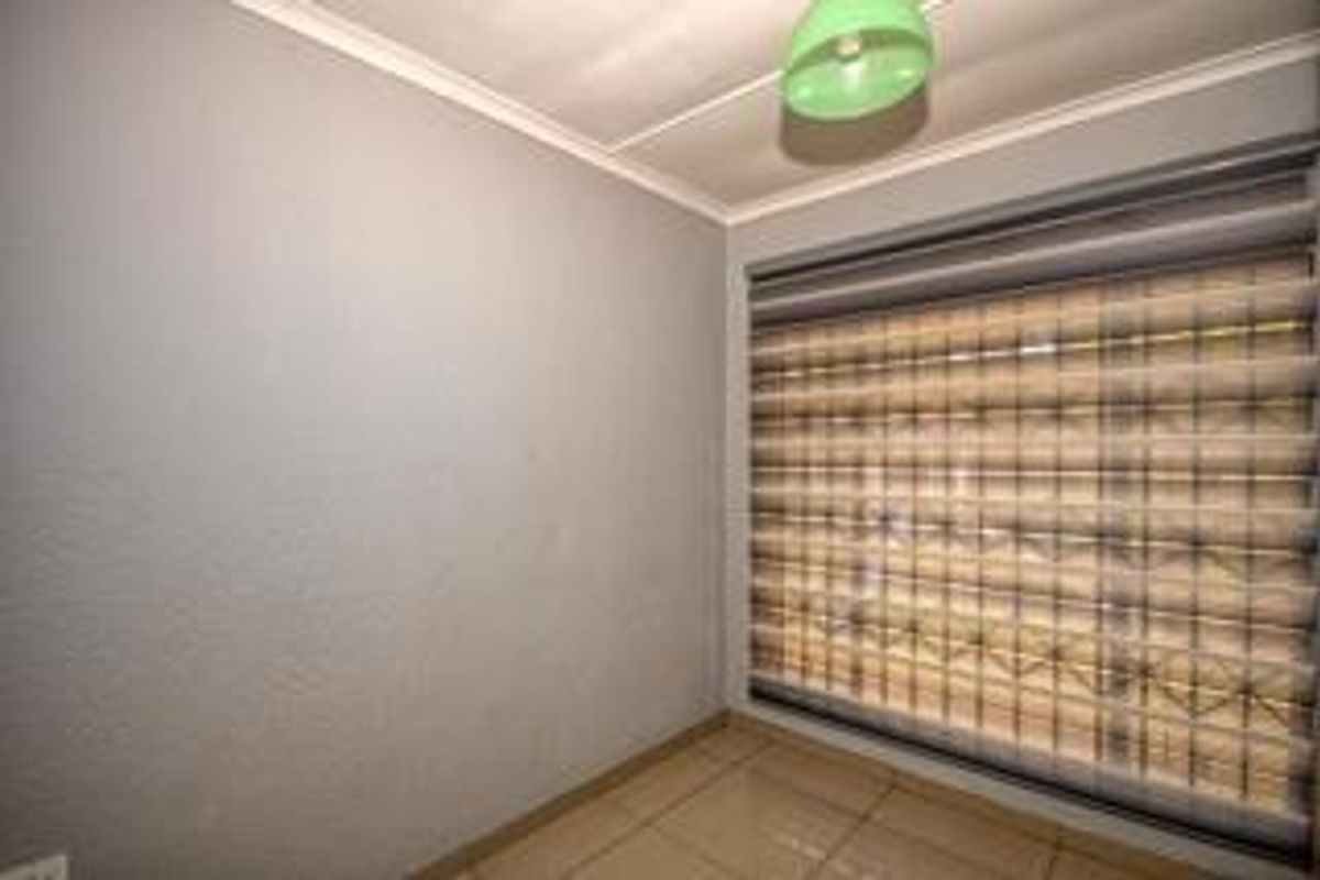 A clean, empty bedroom featuring neutral wall finishes, tiled flooring, and fitted roller blinds, providing a versatile space ready for personalization.