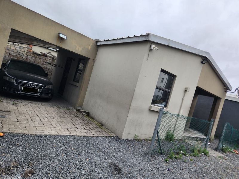 Front exterior view of the property featuring a paved carport, gravel driveway, and perimeter fencing with visible signs of exterior wear.