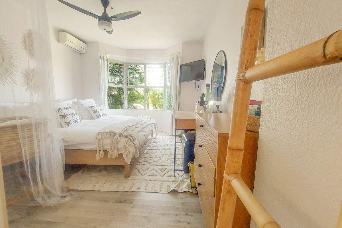 A bright bedroom featuring a bay window, ceiling fan, and wall-mounted air conditioning unit with light-toned wood-look flooring.