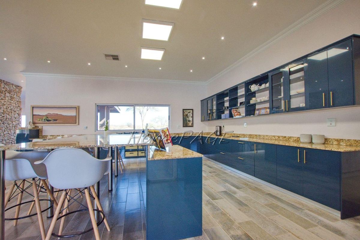 Modern kitchen featuring high-gloss blue cabinetry, granite countertops, a large central island, and recessed ceiling lighting.