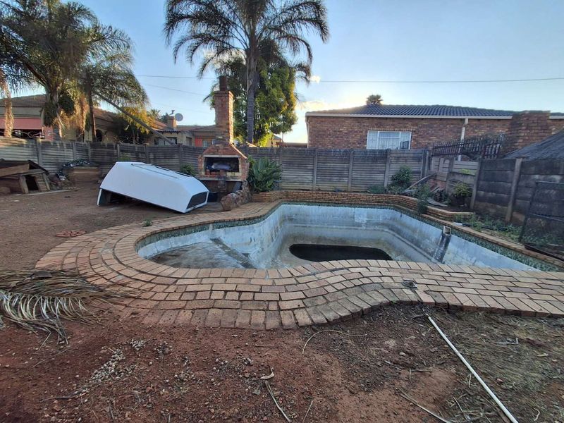 Outdoor pool area featuring a brick-paved surround, a built-in brick braai, and a swimming pool requiring maintenance and refurbishment.