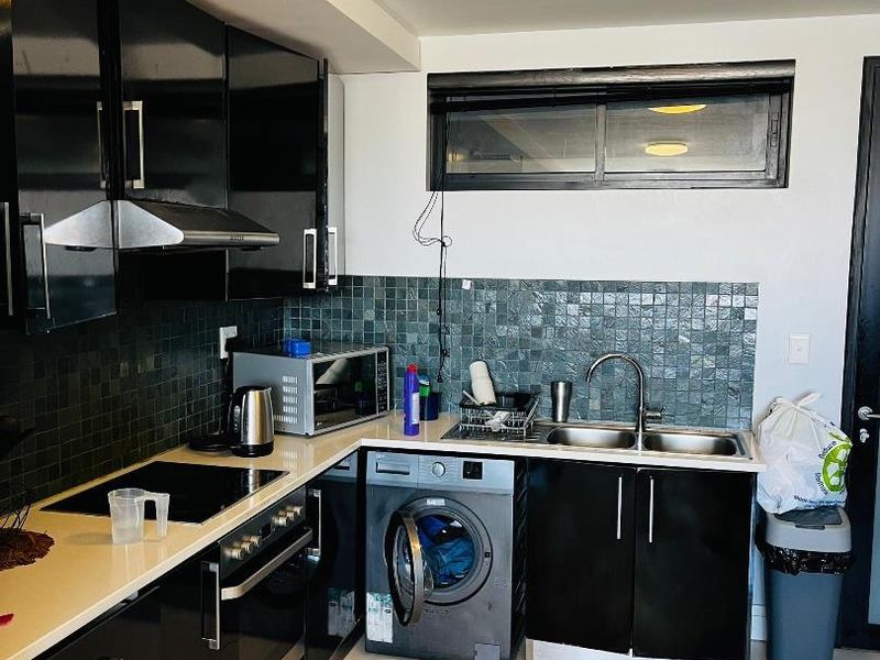 Modern kitchen featuring black gloss cabinetry, stone countertops, mosaic tile backsplash, built-in oven, electric hob, and an integrated washing machine.