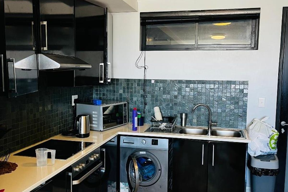 Modern kitchen featuring black gloss cabinetry, stone countertops, mosaic tile backsplash, built-in oven, electric hob, and an integrated washing machine.