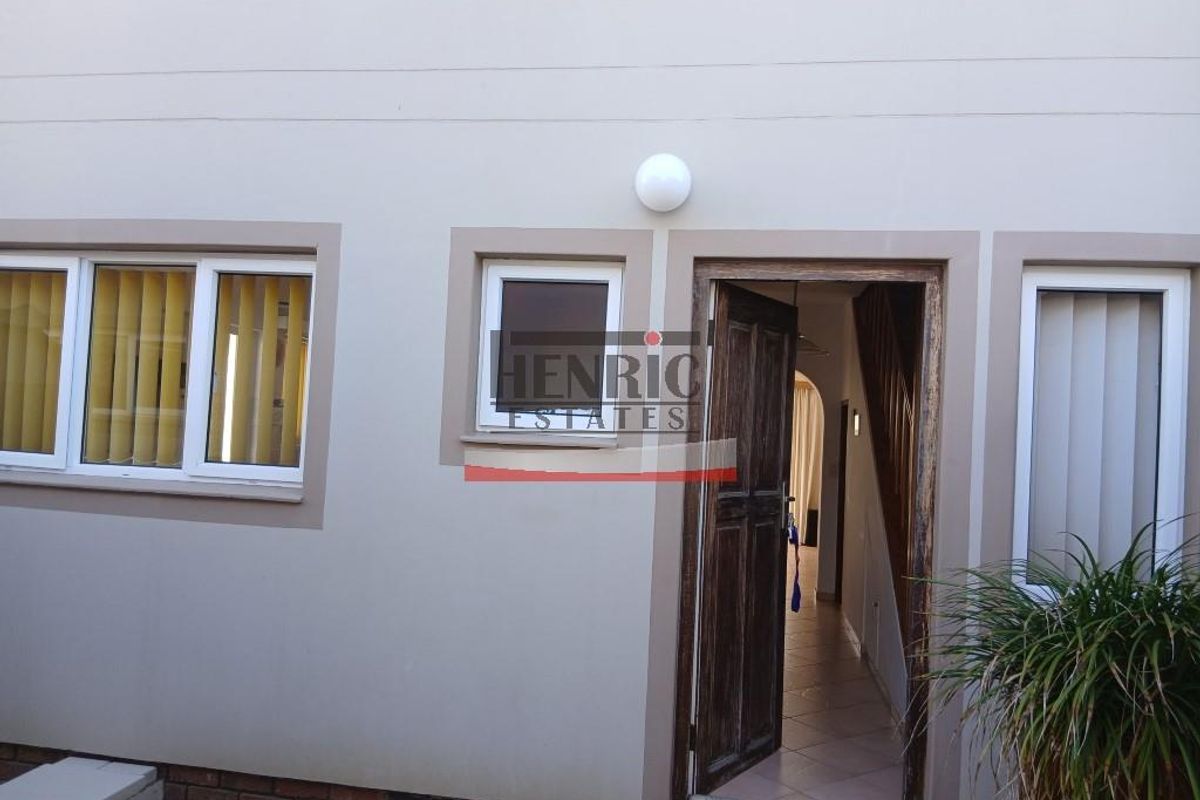 Rear exterior view of the townhouse featuring a timber entrance door, uPVC window frames, and exterior wall lighting.