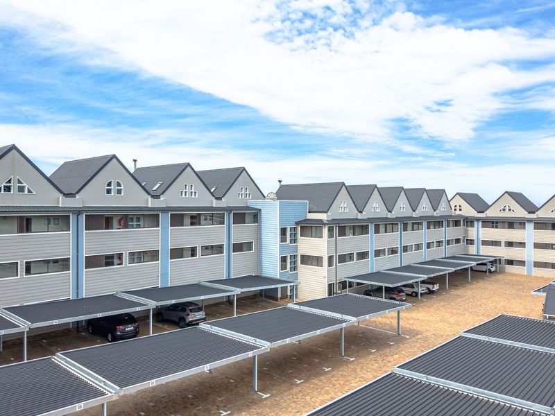Aerial view of a multi-story apartment complex featuring extensive covered parking bays and paved driveway areas.