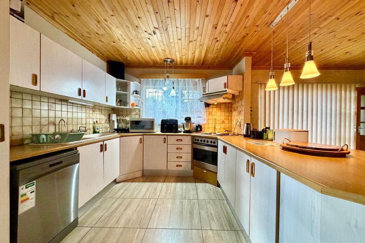 A functional kitchen featuring light-toned cabinetry, tiled backsplash, integrated oven and hob, and a timber-clad ceiling with pendant lighting.