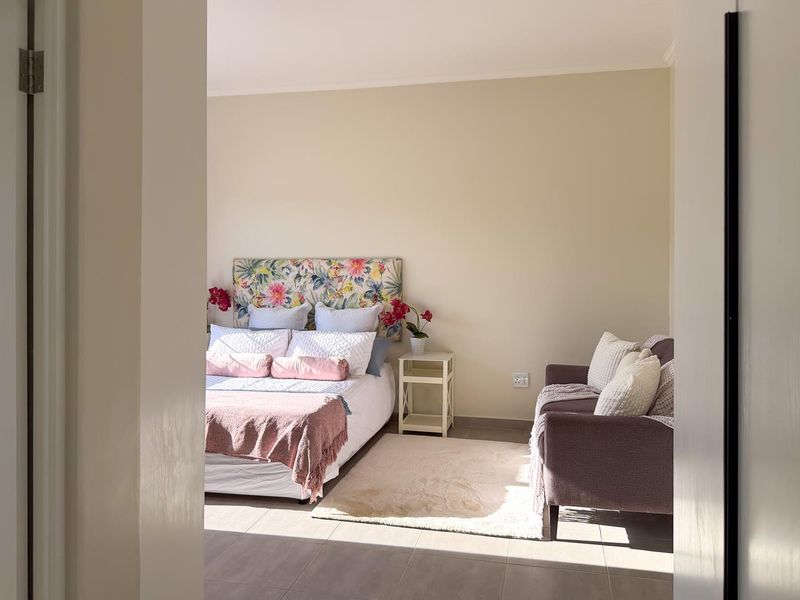 A well-lit bedroom featuring neutral wall tones and tiled flooring, viewed through a doorway.