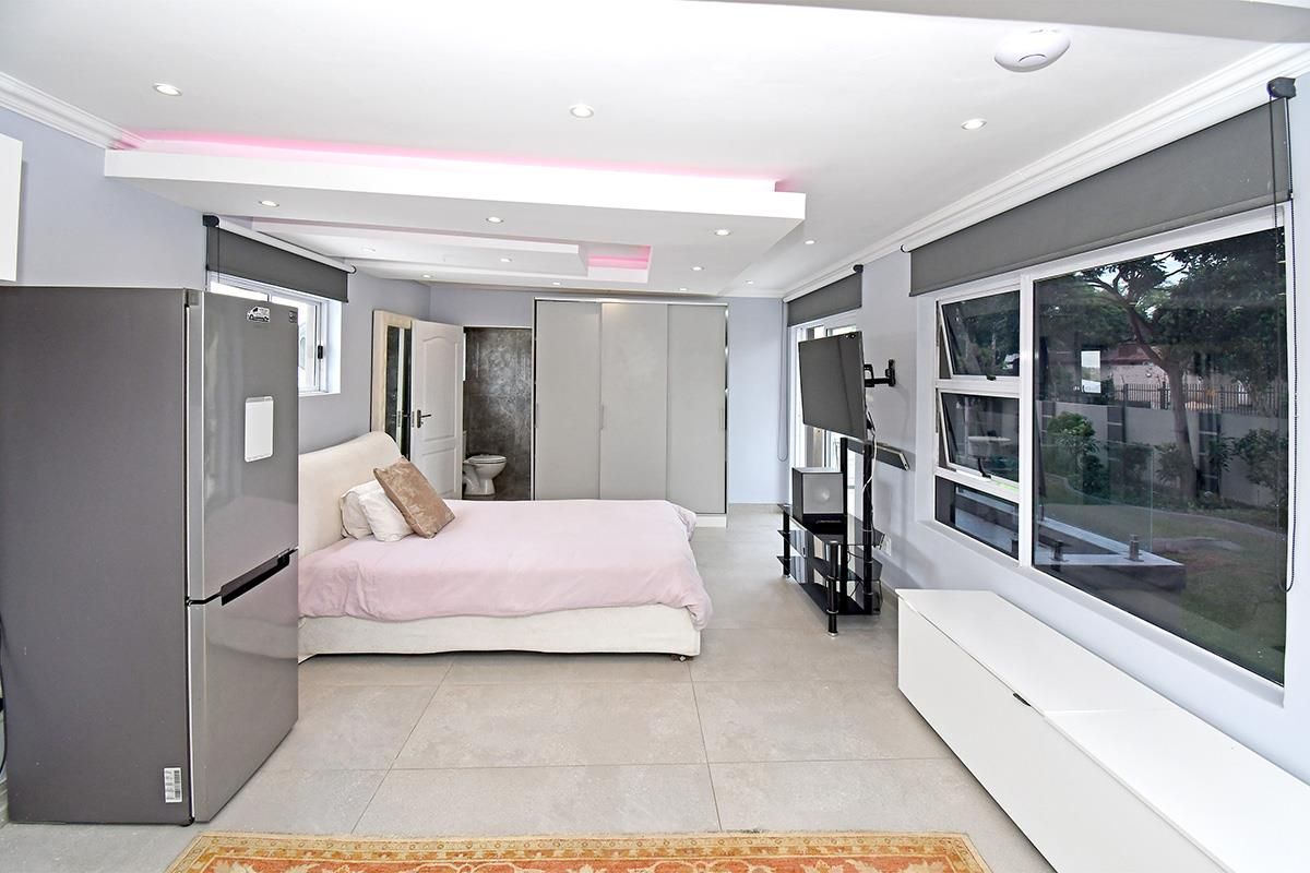 Spacious bedroom featuring large format floor tiles, built-in cupboards, recessed ceiling lighting with ambient features, and large windows providing natural light.