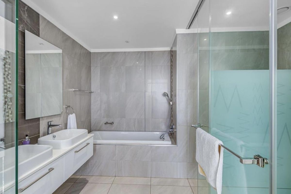 Modern bathroom featuring a double vanity, wall-mounted cabinetry, a built-in bathtub, and a glass-enclosed shower with frosted privacy detailing.