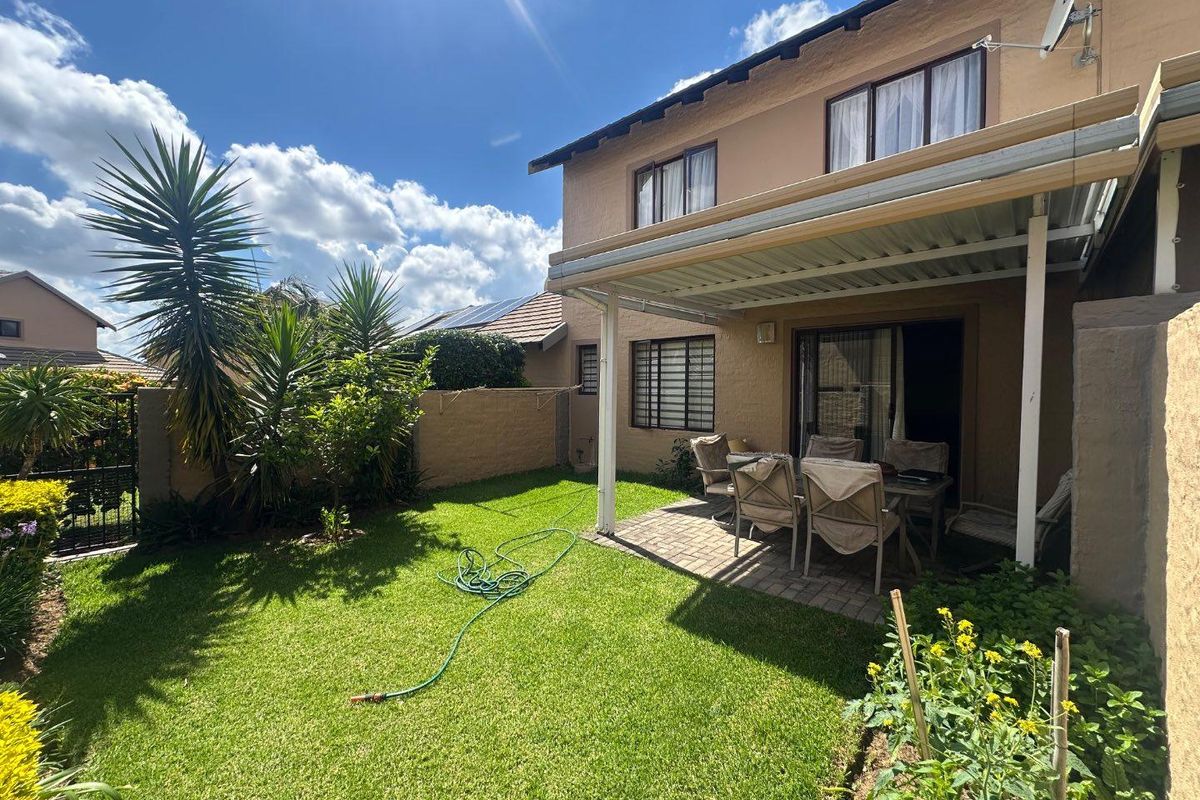Rear view of the townhouse featuring a paved patio area under a metal roof structure, overlooking a private lawn and garden.