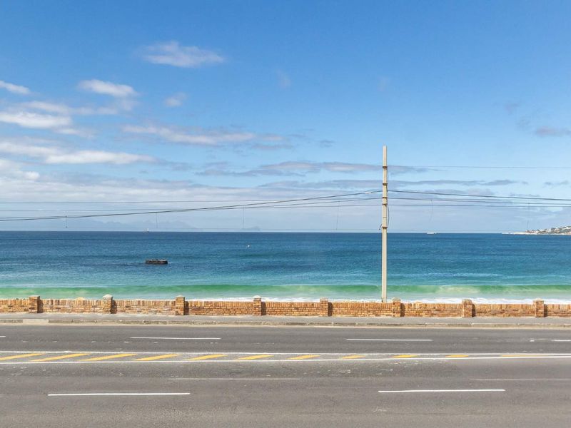 A clear view of the ocean and coastline from the property, featuring a brick boundary wall and adjacent coastal road.