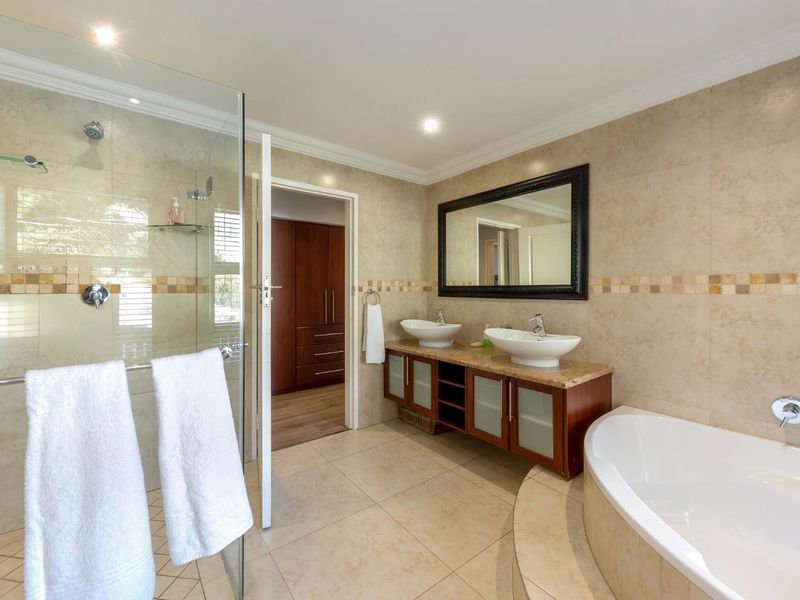 Spacious bathroom featuring a double vanity with vessel sinks, a glass-enclosed shower, and a built-in bathtub with neutral tiled finishes.