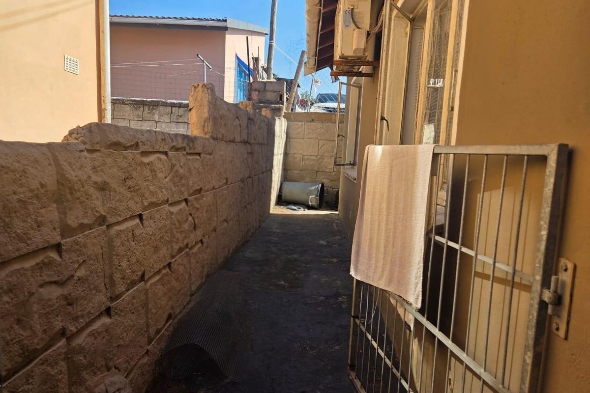 A narrow side passage featuring a stone boundary wall, concrete paving, and an exterior air conditioning unit.