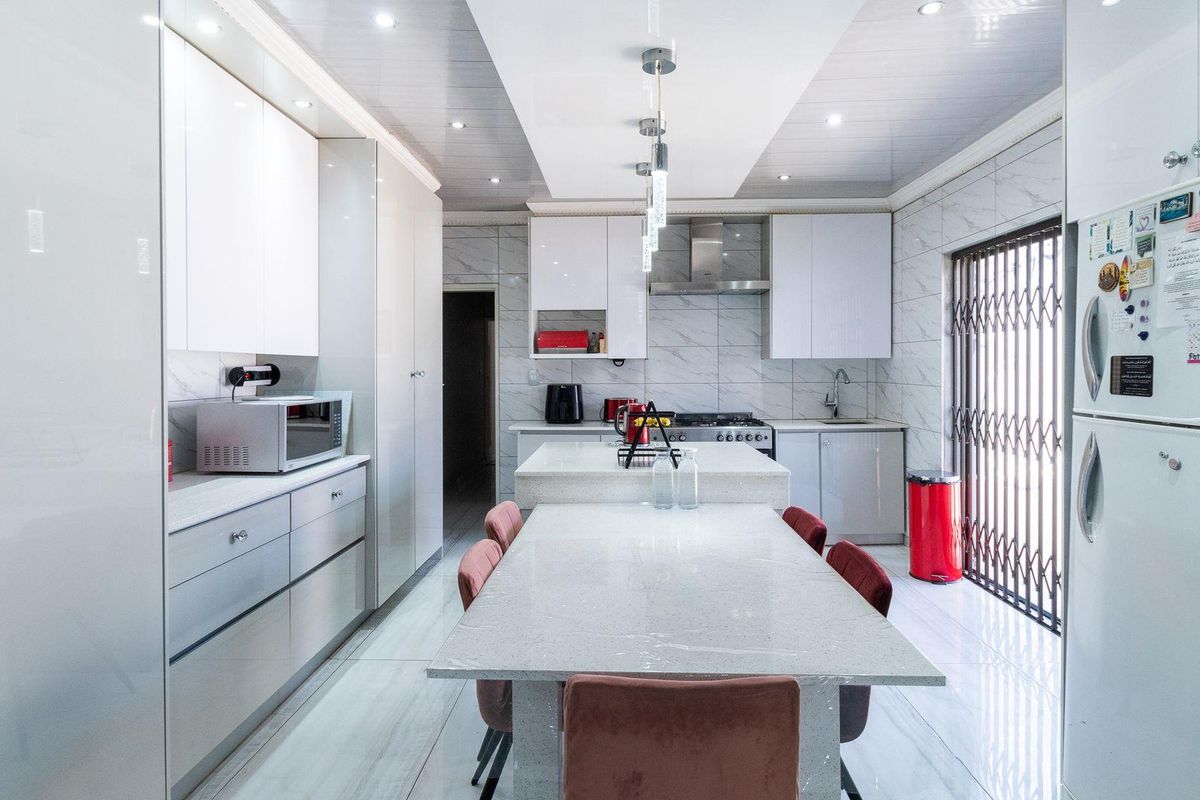 Modern kitchen featuring high-gloss cabinetry, stone countertops, a central island with integrated dining space, and marble-look tiled flooring.