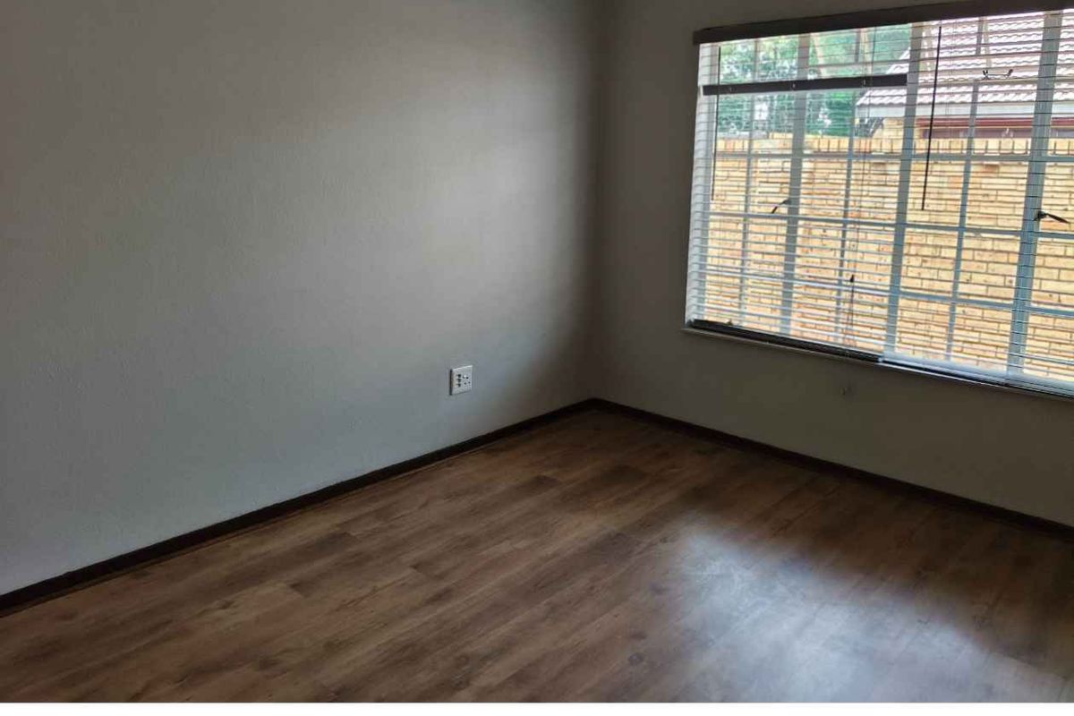 A clean, empty bedroom featuring wood-look laminate flooring and a window with fitted blinds, offering a neutral canvas for personalization.