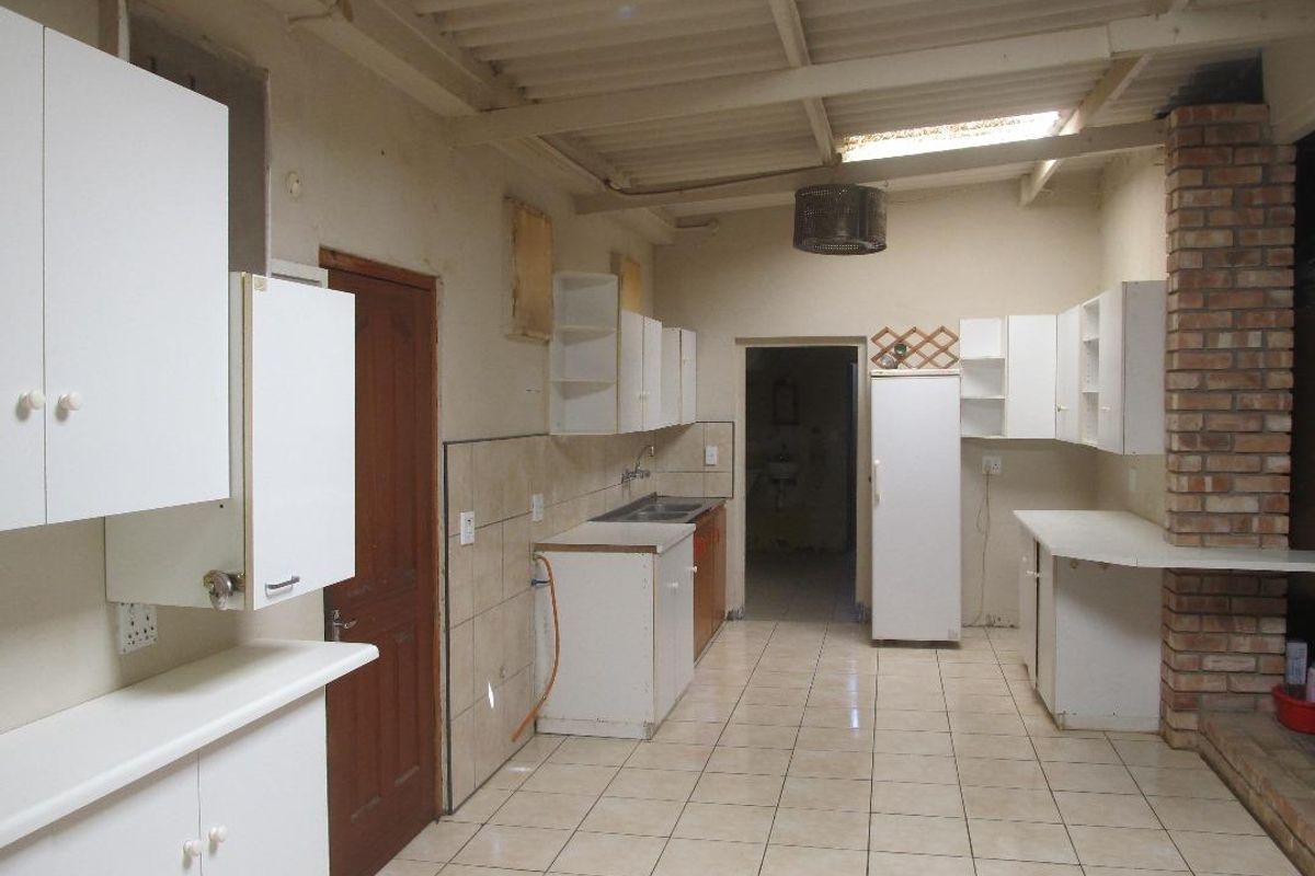 A functional kitchen space featuring white cabinetry, tiled flooring, and an exposed brick pillar, offering a blank canvas for potential renovation and modernization.