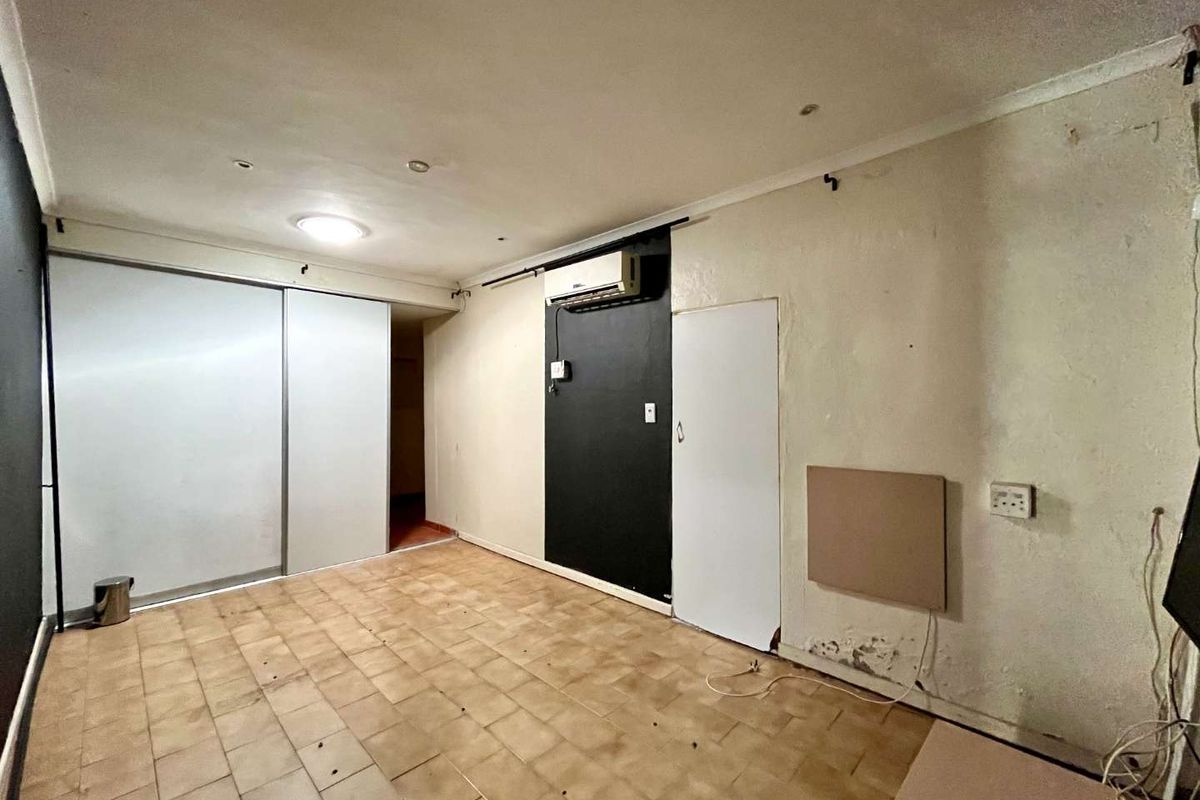 An empty bedroom featuring tiled flooring, a built-in sliding wardrobe, and a wall-mounted air conditioning unit, requiring cosmetic updates and wall repairs.
