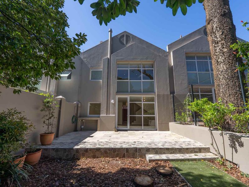 Rear view of the townhouse featuring a stone-paved patio, built-in outdoor braai, and large glass doors leading into the living area.