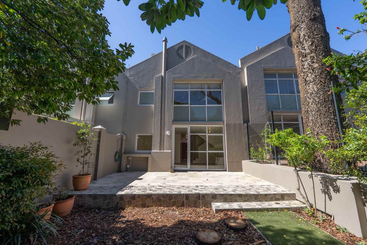 Rear view of the townhouse featuring a stone-paved patio, built-in outdoor braai, and large glass doors leading into the living area.