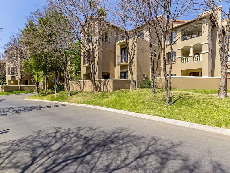 A view of the apartment complex exterior featuring multi-story units with balconies, a landscaped lawn, and paved street access.