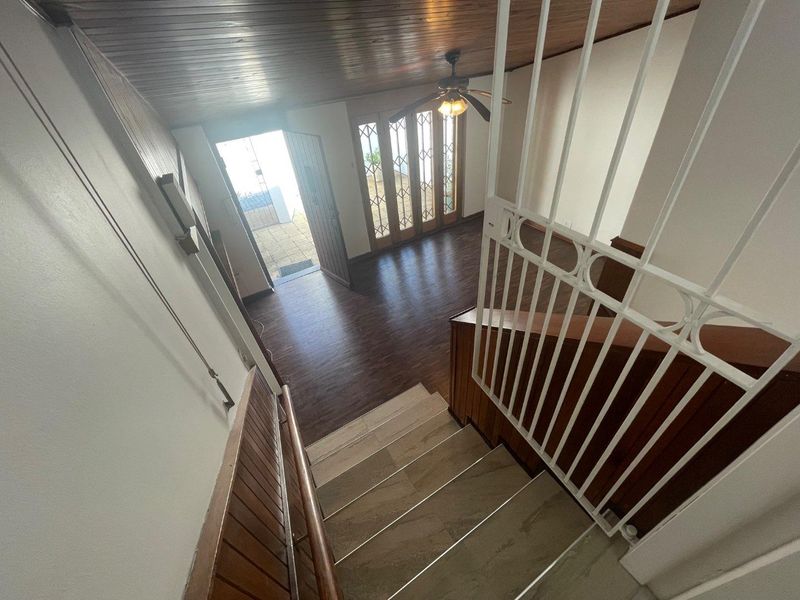 An entry area featuring a timber ceiling, tiled staircase with security gate, and timber-framed glass doors leading to an outdoor space.