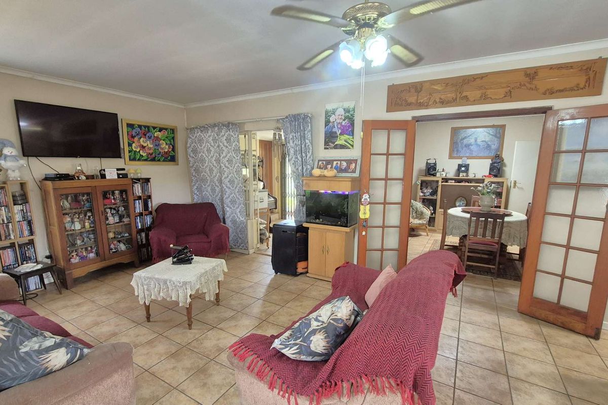 Spacious living area featuring tiled flooring, a ceiling fan, and double wooden doors leading to an adjacent dining room.