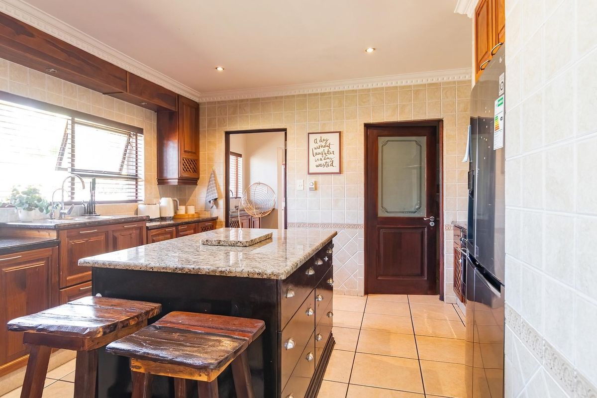 A well-maintained kitchen featuring wooden cabinetry, granite countertops, a central island, and tiled finishes throughout.