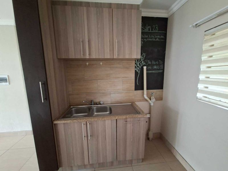 A functional laundry area featuring wood-look built-in cabinetry, a double stainless steel sink, tiled backsplash, and dedicated plumbing connections.