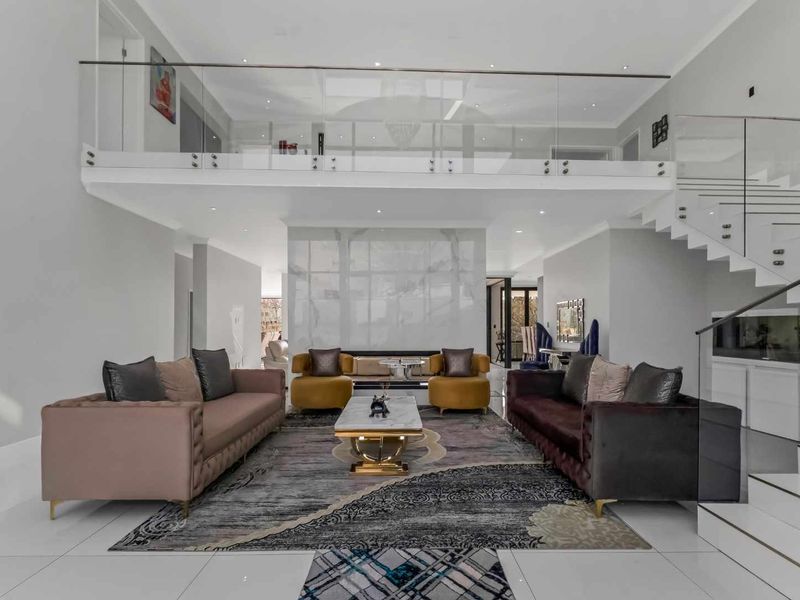 Spacious double-volume living area featuring a striking marble feature wall, glass balustrade mezzanine, and modern floating staircase with high-gloss tiled flooring.
