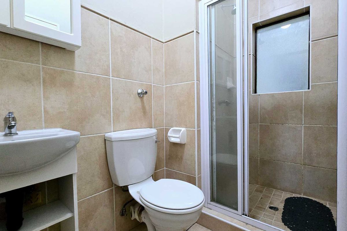 A compact bathroom featuring a tiled shower enclosure, a standard toilet, and a wall-mounted basin with storage underneath.