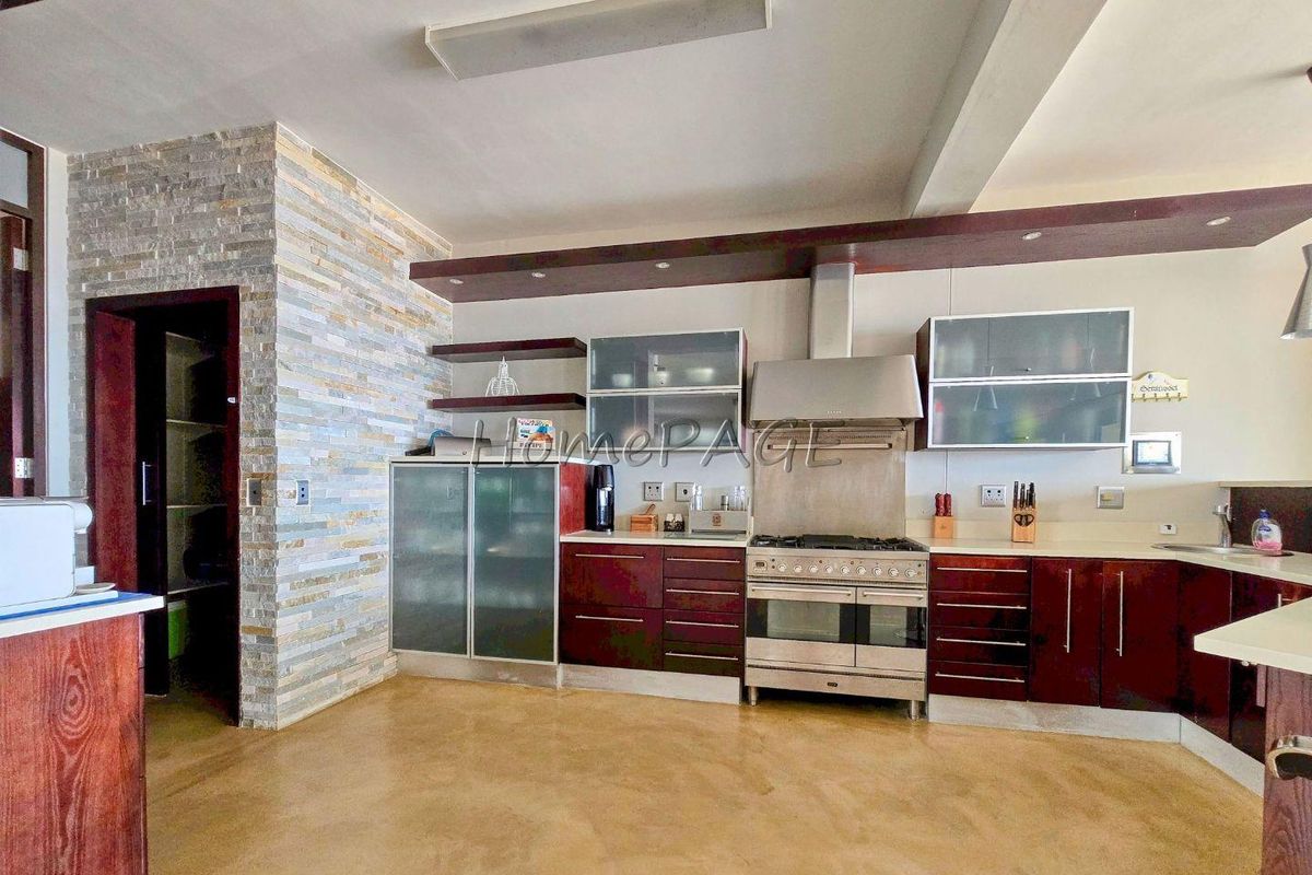 Spacious kitchen featuring dark wood cabinetry, stainless steel gas range with extractor fan, stone-clad feature wall, and ample counter space.