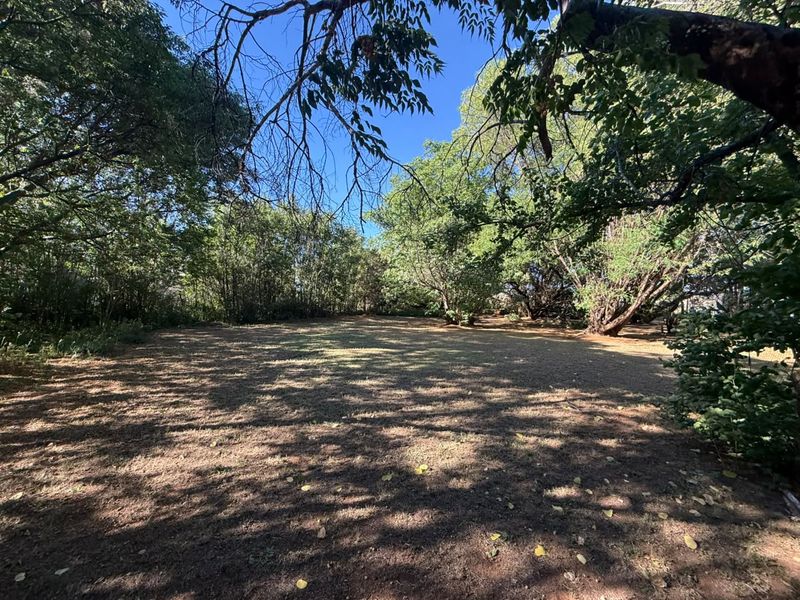 A spacious, tree-lined garden area featuring mature trees and established grounds, offering a private and natural outdoor setting.
