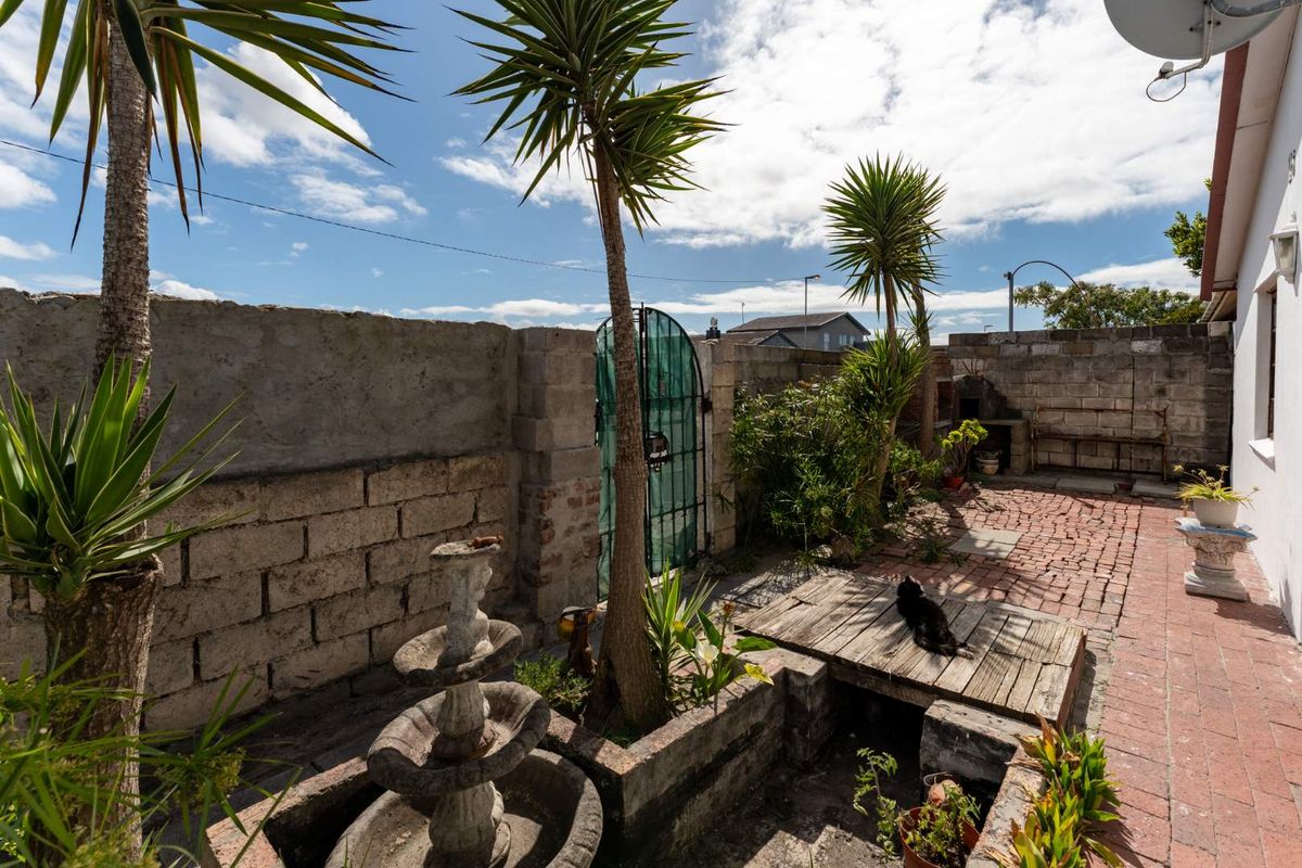 A private rear courtyard featuring brick paving, concrete block boundary walls, a built-in masonry barbecue area, and established garden landscaping.