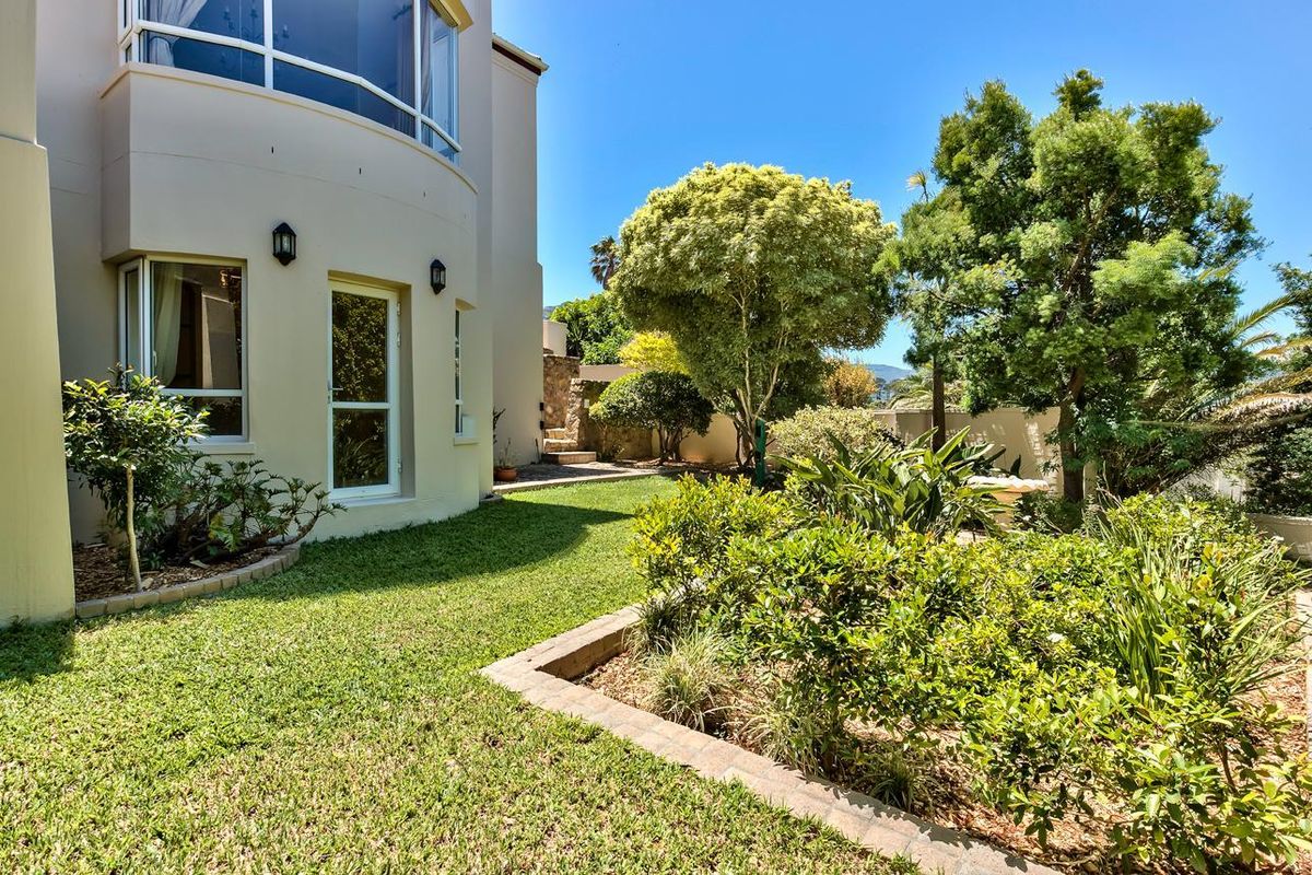 A well-maintained rear garden featuring a lush lawn, established trees, and brick-edged garden beds adjacent to the curved rear facade of the house.