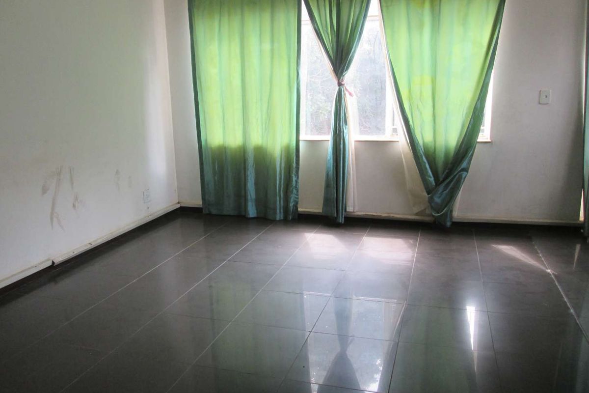 An empty living room featuring dark tiled flooring and a large window with green curtains, requiring minor cosmetic updates to the walls.