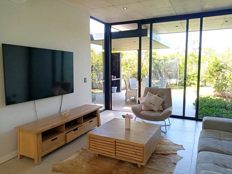 Modern living room featuring an exposed concrete ceiling, large sliding glass doors providing seamless indoor-outdoor flow, and neutral tiled flooring.